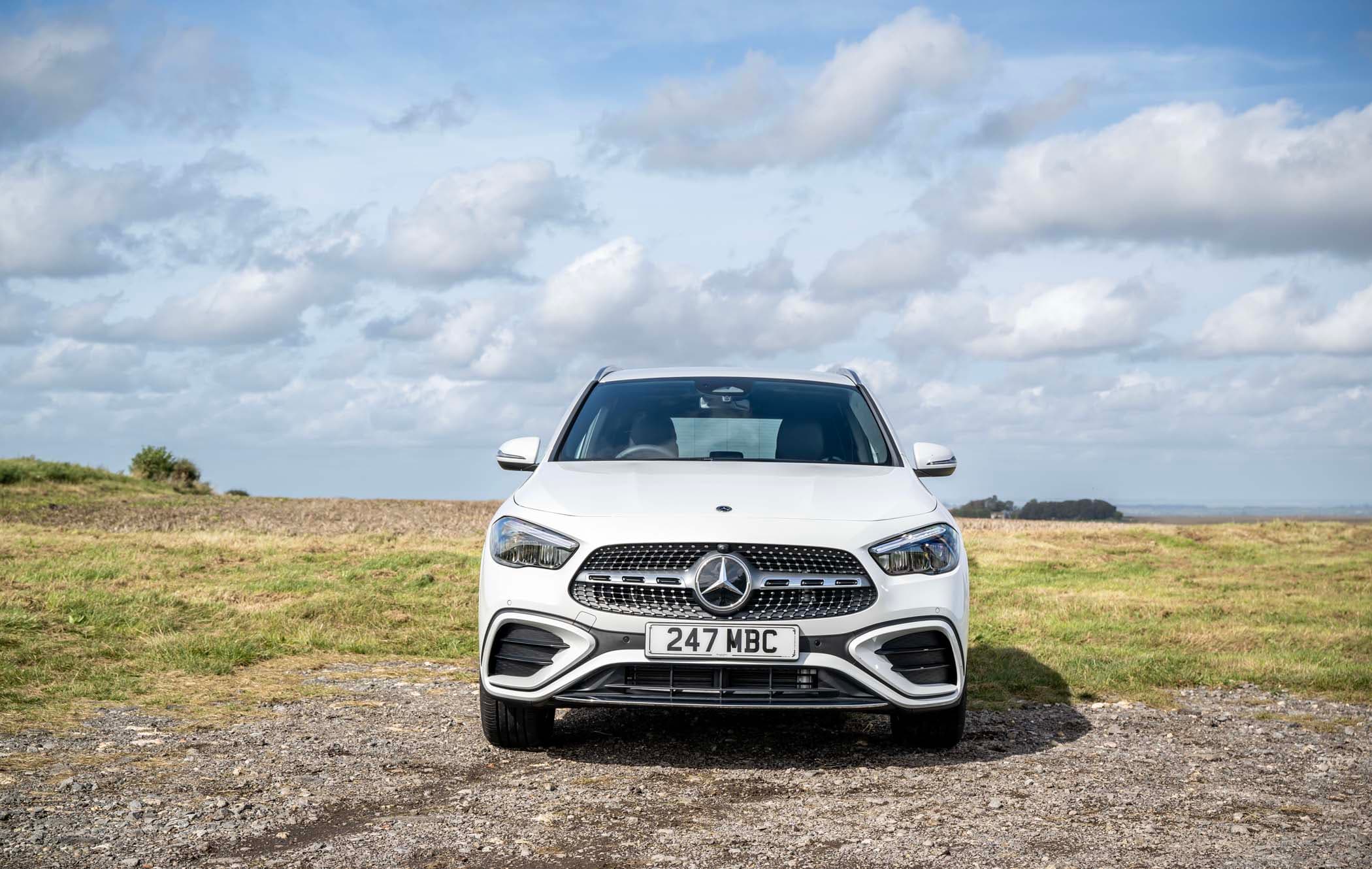 A white Mercedes GLA parked on a grassy field under a partly cloudy sky.